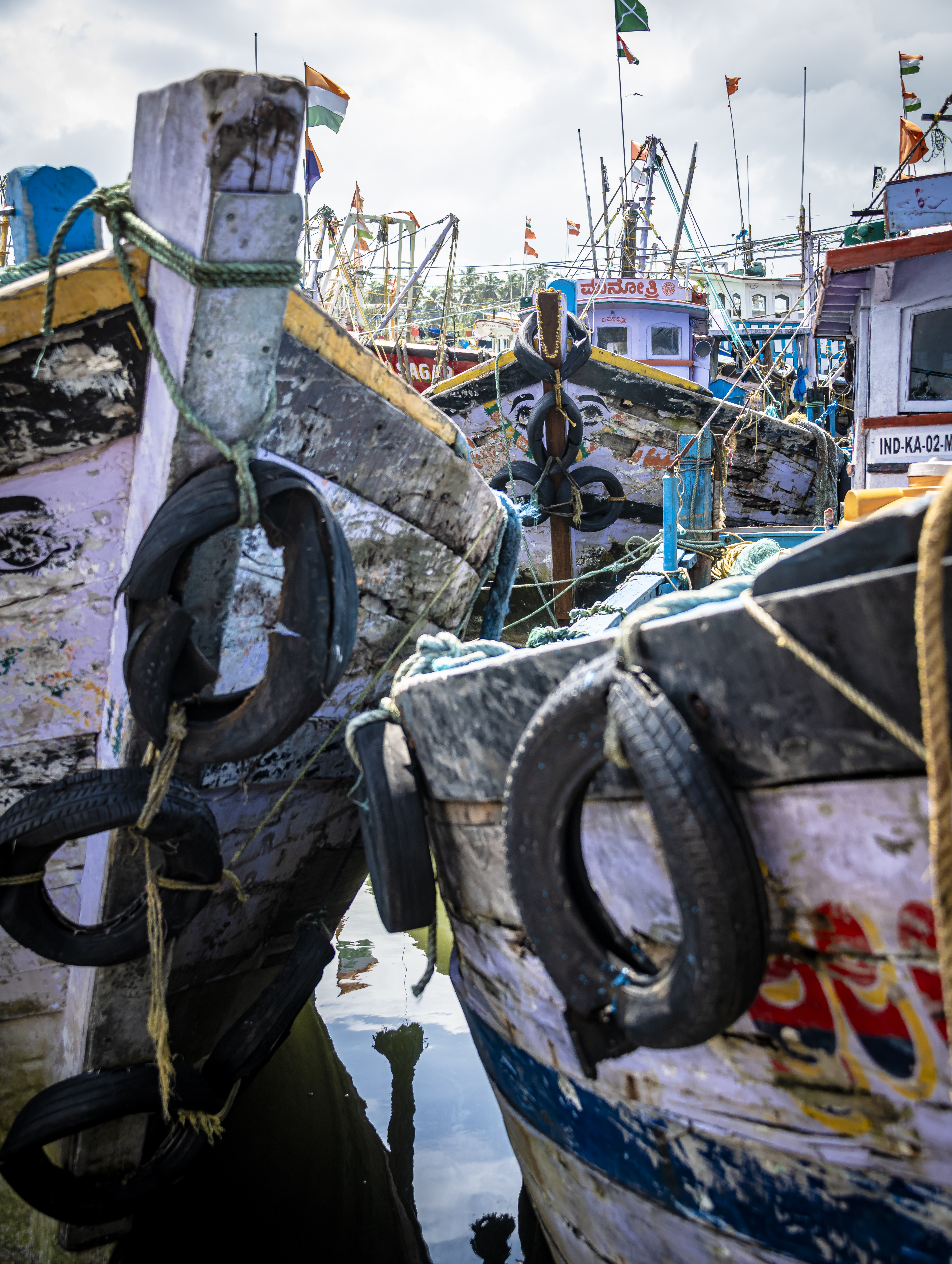 Close-up view of several fishing boats docked in a harbor, showing colorful flags and reflections in the water.